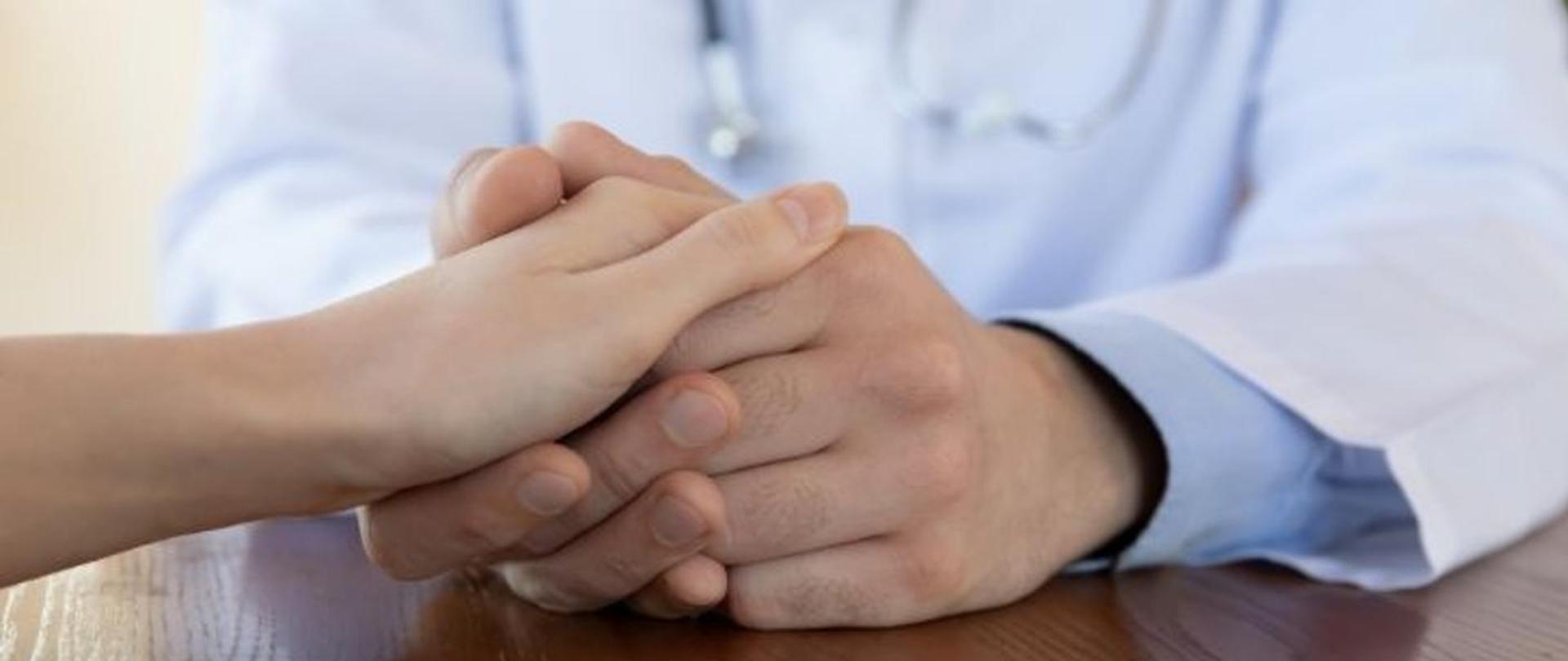 Lekarz trzymający pacjenta za rękę i najprawdopodobniej udzielający mu wsparcia