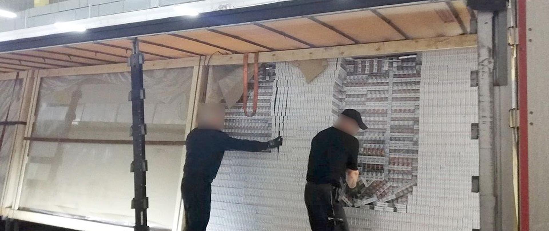 Funkcjonariusze KAS wewnątrz naczepy podczas wyjmowania ukrytych nielegalnych papierosów.