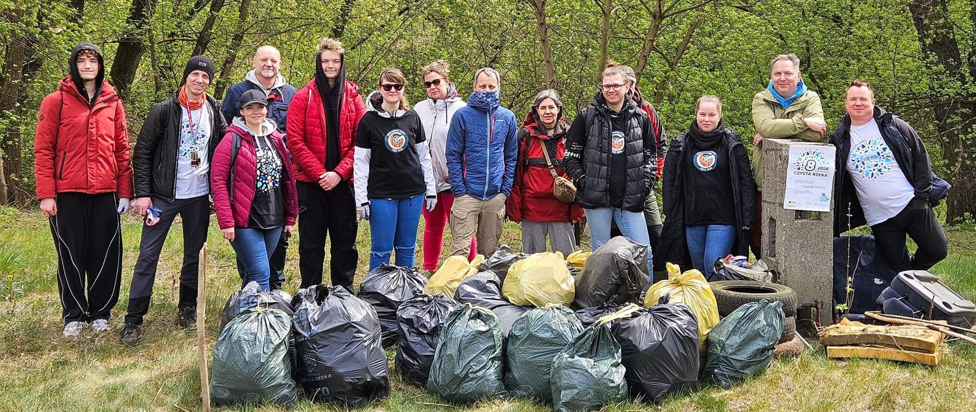 grupa ludzi w terenowych strojach patrz w obiektyw. Przed nimi leżą worki z odpadami. 
