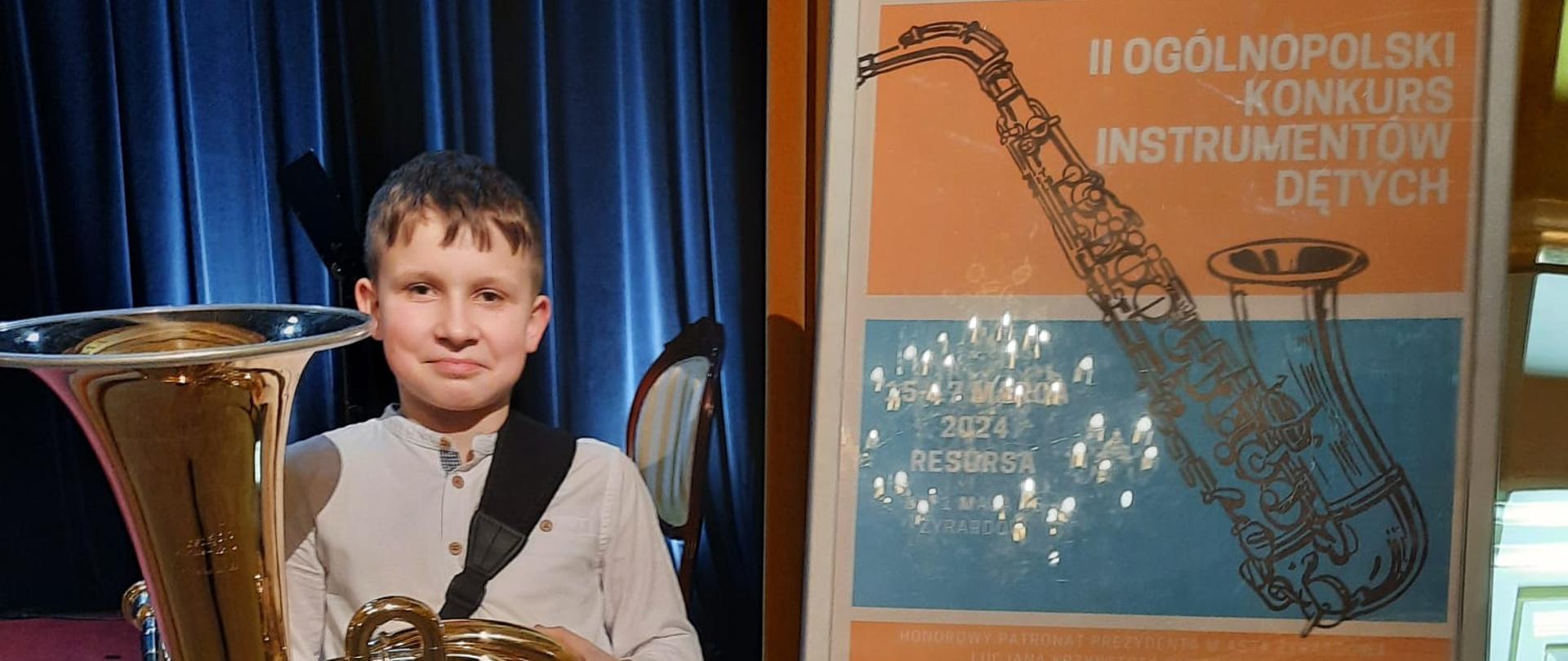 Zdjęcie przedstawia stojącego z tubą, ucznia Tomasza Weinkopfa, obok po prawej plakat konkursu