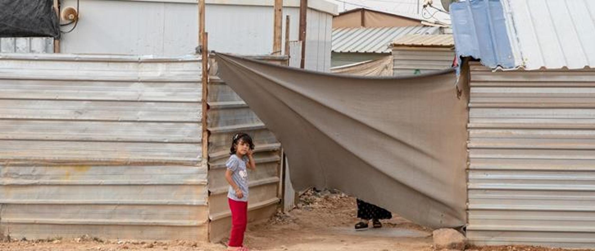 Small girl standing at the entrance of fence made of tinware