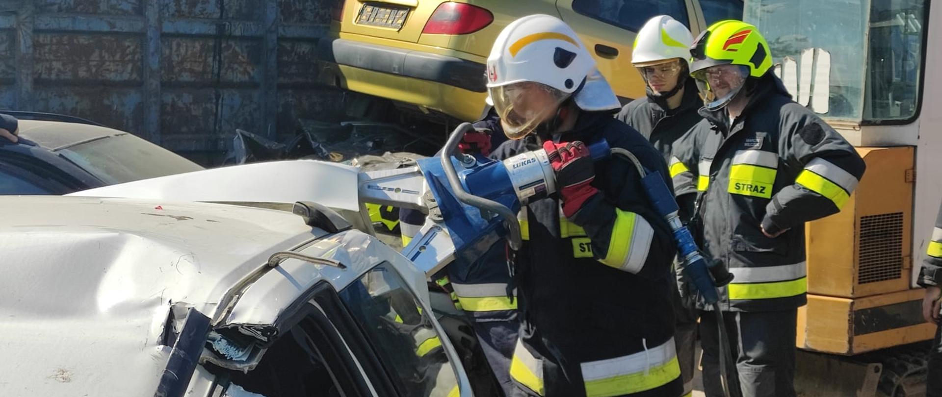 Druhowie OSP ubrani w ubrania specjalne, hełmy ćwiczący użycie rozpieracza hydraulicznego.