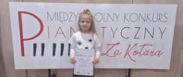 Klara Utrata stoi na tle planszy konkurs pianistyczny za kotarą