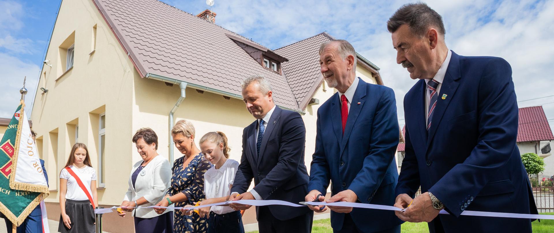
Grupa ludzi stojąca na placu przed szkołą