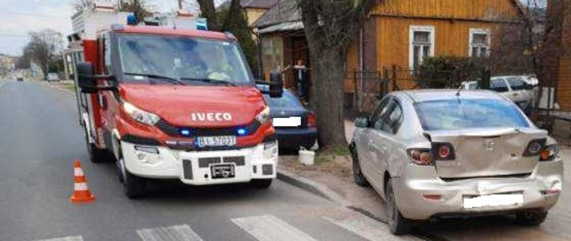 Samochód osobowy koloru srebrnego z uszkodzonym tyłem pojazdu, za nim samochód pożarniczy.