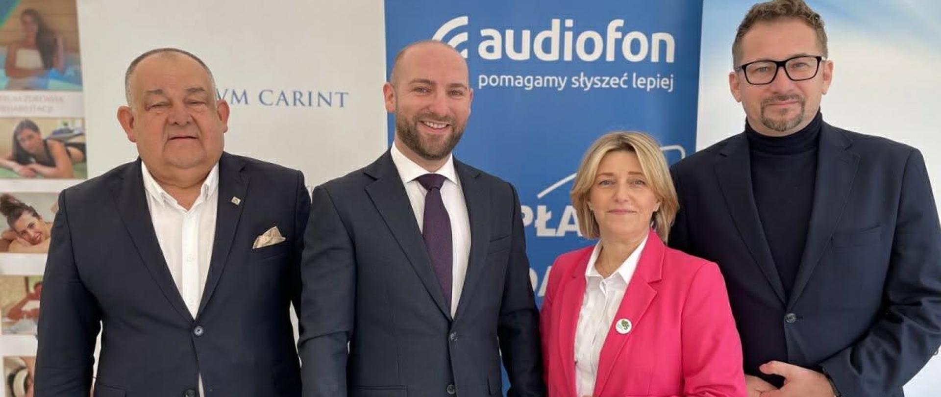 Osoby pozują do zdjęcia, za nimi znajdują się roll-upy partnerów wydarzenia.
