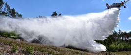 Zdjęcie przedstawia zrzut wody samolotu pożarniczego na ognisko pożaru w trakcie ćwiczeń powiatowych