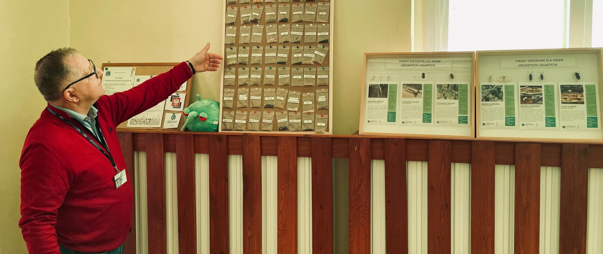 Zdjęcie przedstawia inspektora pokazującego tablicę oraz jej zawartość w postaci nasion