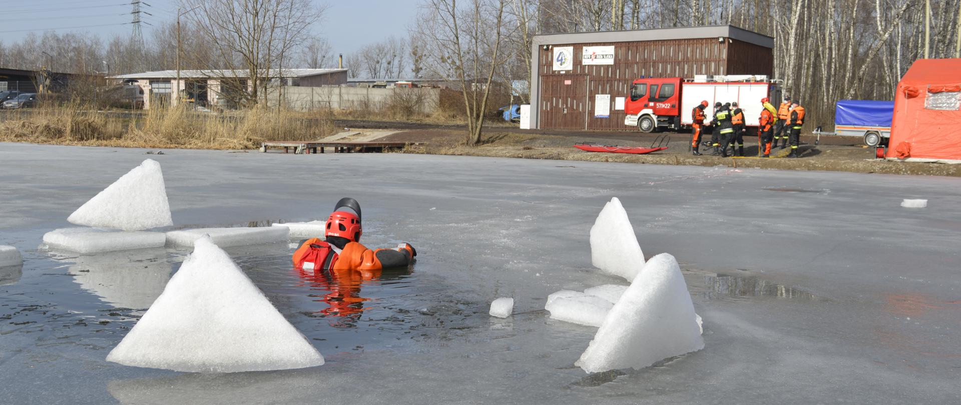 Strażak w przeręblu w tle strażacy oraz samochód gaśniczy