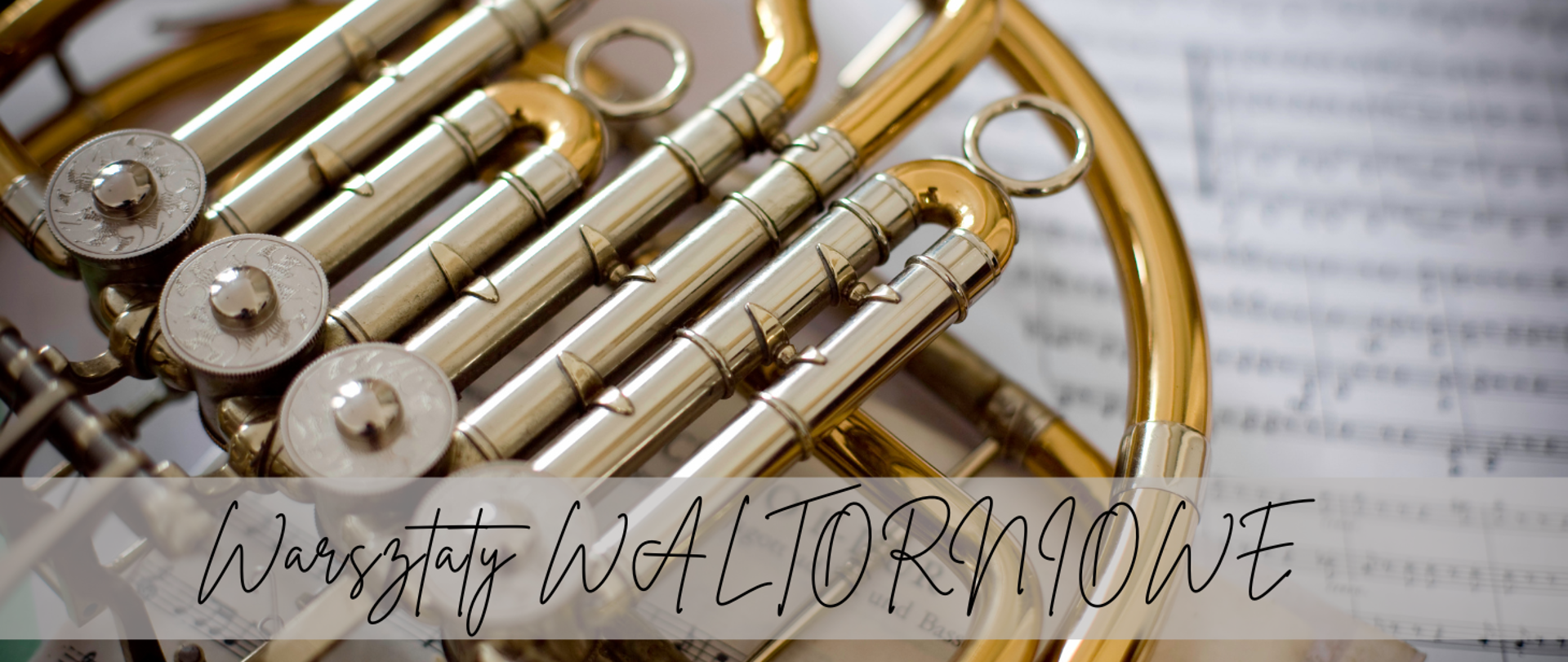 Na obrazku widać fragment waltorni (rogu francuskiego). W tle znajduje się rozłożony arkusz z nutami. Na dole obrazu widnieje napis w ozdobnej, odręcznej czcionce: „Warsztaty WALTORNIOWE”. Kolorystyka jest ciepła, z dominującymi odcieniami złota i beżu.