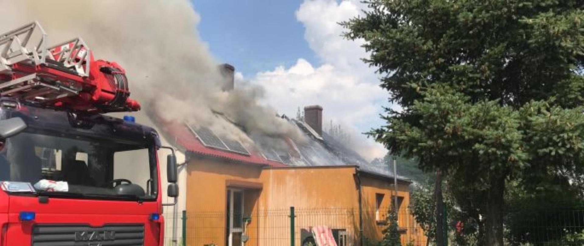 Samochód z wysięgnikiem hydraulicznym na tle palącego się dachu budynku mieszkalnego