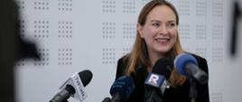 Minister funduszy i polityki regionalnej Katarzyna Pełczyńska-Nałęcz stoi przy mikrofonach i się uśmiecha