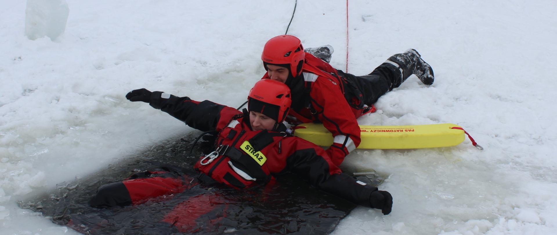 strażak wyciąga z przerębli pozoranta przy użyciu pasa ratowniczego. Strażak leży zabezpieczony linką ratowniczą