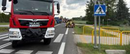 Na zdjęciu widać fragment drogi. Widać auto po wypadku oraz oraz dwa wozy strażackie i samochód ciężarowy. Widać strażaków zabezpieczających auto osobowe. 