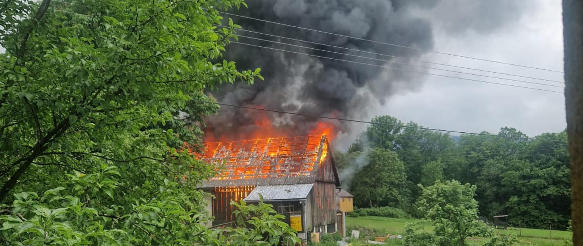 Płonący budynek gospodarczy. Płomienie wychodzą ponad dach.