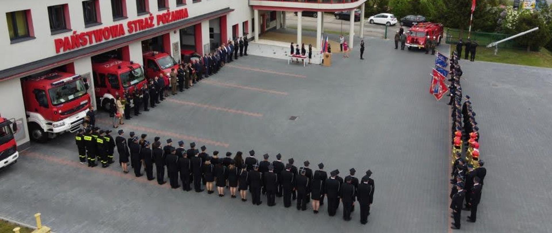 Na zdjęciu znajdują się funkcjonariusze KP PSP w Chełmnie, druhny i druhowie OSP z powiatu chełmińskiego, poczty sztandarowe oraz zaproszeni goście. Zdjęcie wykonano na placu zewnętrznym przed komendą powiatową.