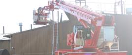 Podnośnik hydrauliczny rozstawiony przed budynkiem, w którym miał miejsce pożar. W koszu podnośnika strażak.