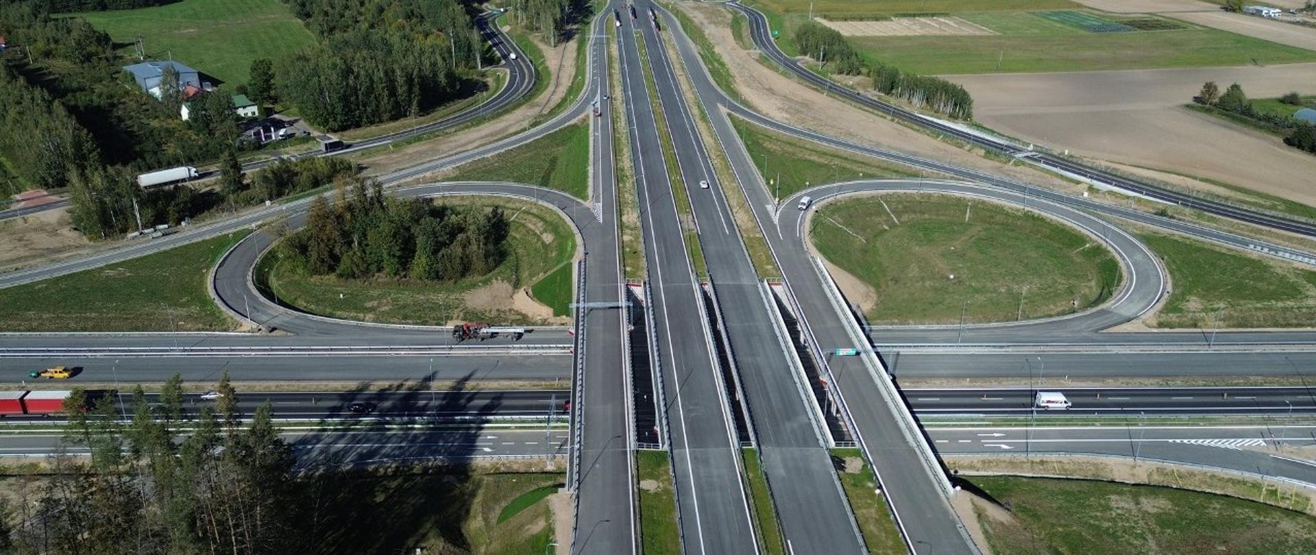 Widok z lotu ptaka na skrzyżowanie autostrad, z wyraźnie widocznymi pasami ruchu i pojazdami.