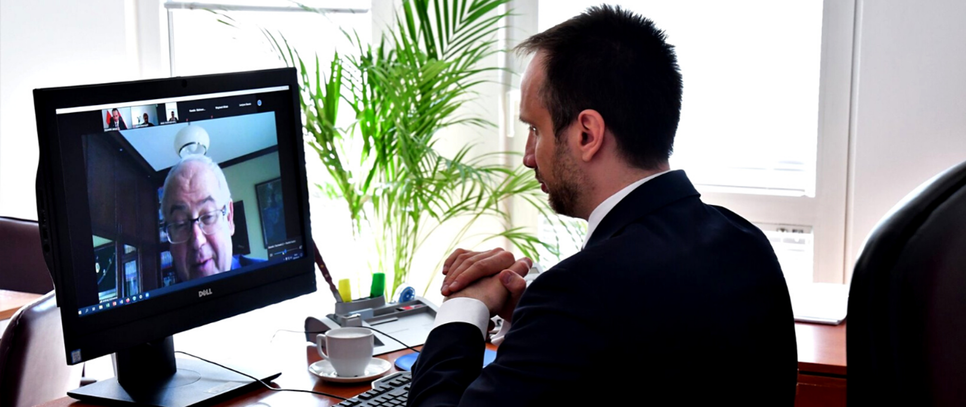 Minister Janusz Kowalski siedzi przy biurku podczas spotkania online. Na ekranie monitora wizerunek prof. Andrzeja Szumańskiego