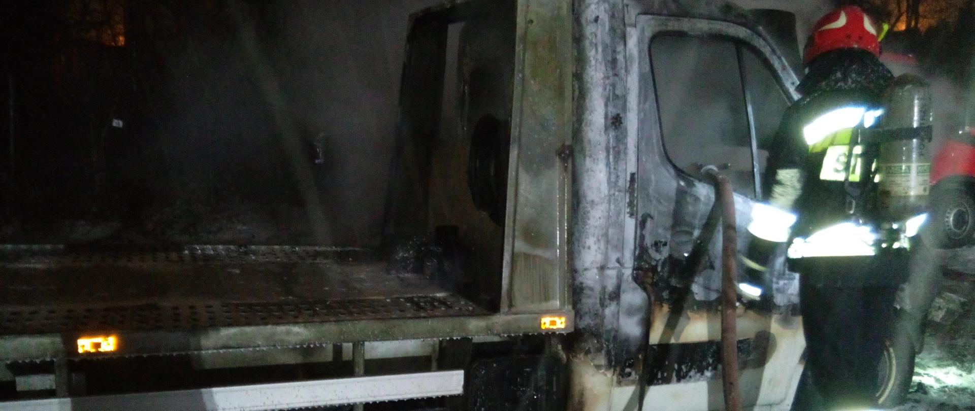 Na zdjęciu widzimy samochód typu laweta zniszczony przez pożar. Na pierwszym planie ratownik.