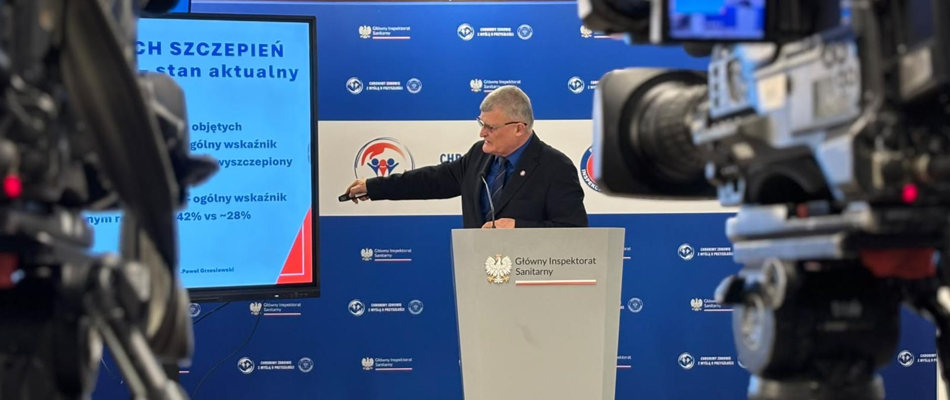 mężczyzna stojący za mównicą, pokazuje prezentację na ekranie
