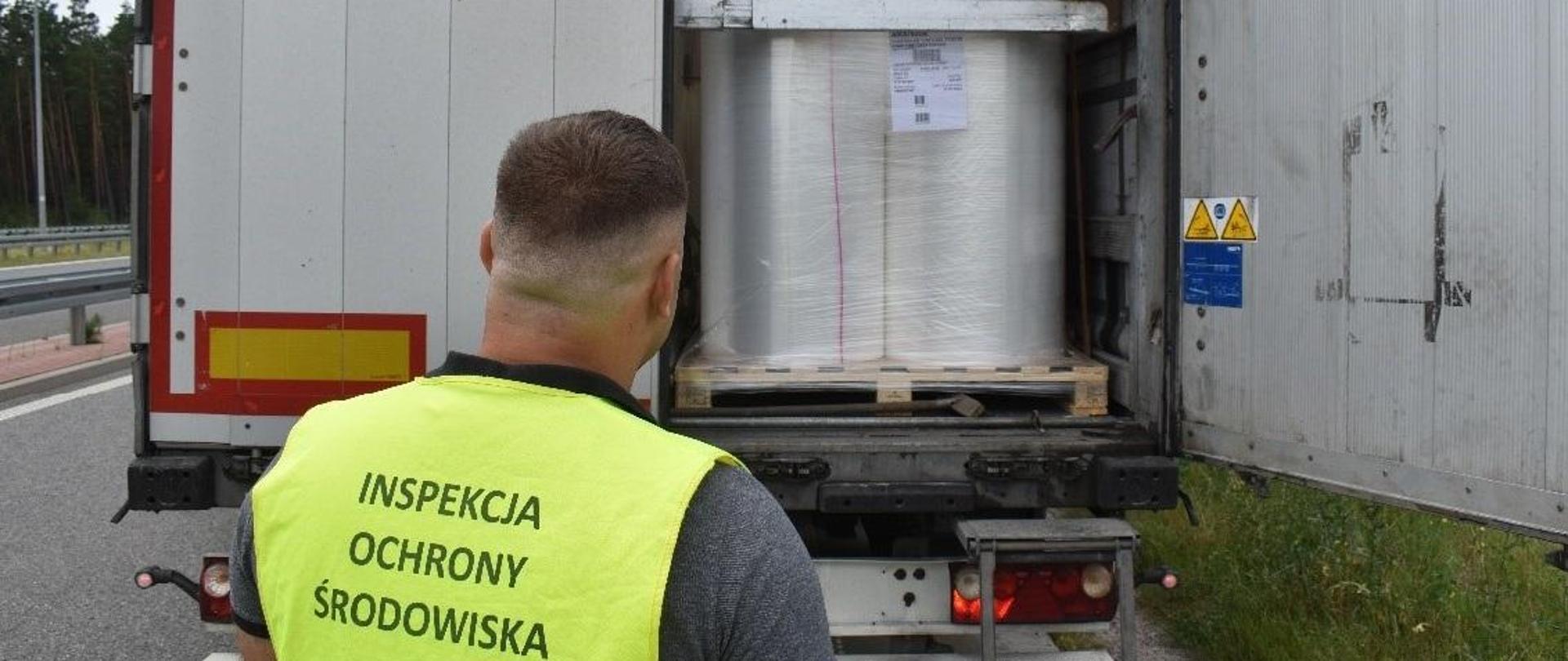 Inspektor Wojewódzkiego Inspektoratu Ochrony Środowiska w Warszawie kontroluje wnętrze naczepy samochodu ciężarowego. Znajduje się w niej wysoka na ok. 1 metr bela folii spożywczej.
