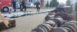 Na placu KP PSP Radomsko ustawiony sprzęt strażacki: hełmy, ubrania specjalne, węże pożarnicze.