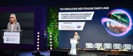 Ministra Klimatu i środowiska Paulina Hennig-Kloska na inauguracji konferencji Ministerstwa Klimatu i Środowiska na terenie Międzynarodowych Targów Poznańskich. Ministra stoi za mównicą, za nią w tle telebim z tytułem konferencji i jej twarzą. 