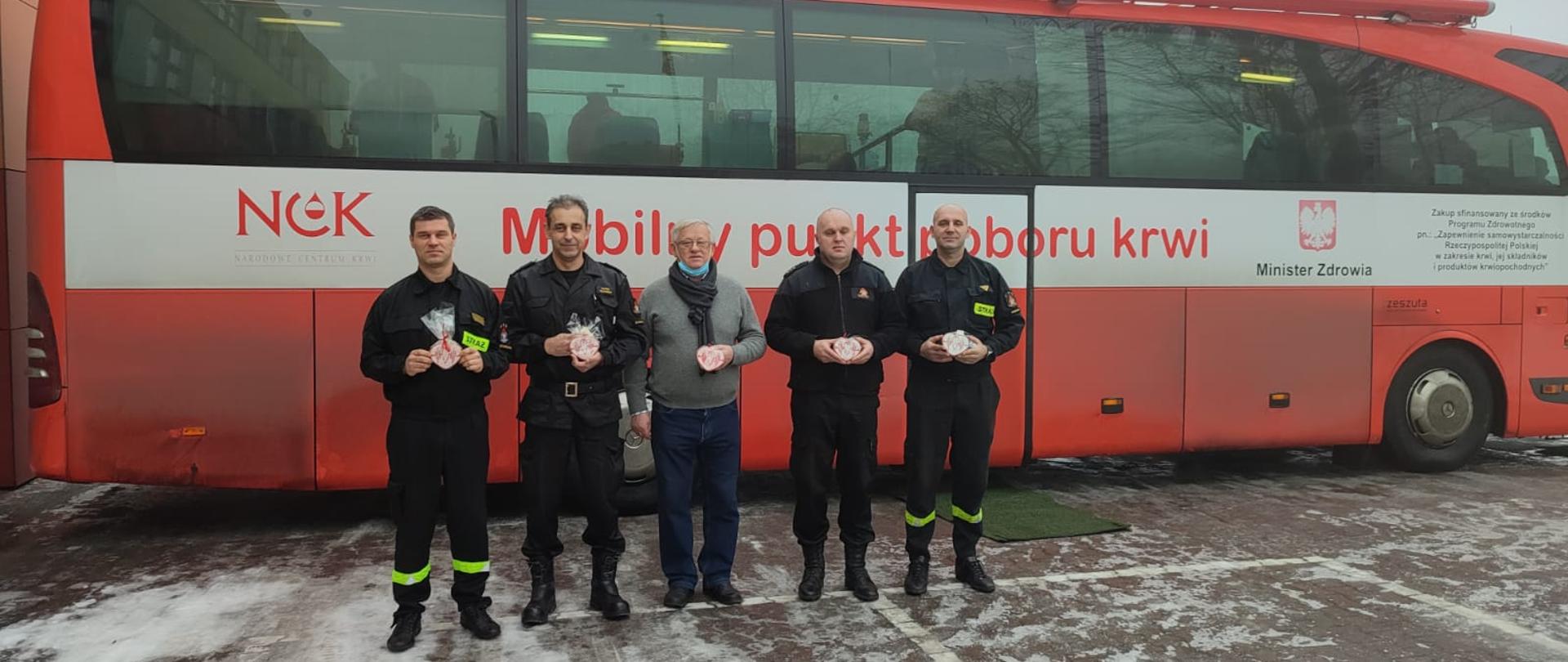 Przed mobilnym punktem poboru krwi stoi pięciu ludzi trzymając piernikowe serduszka