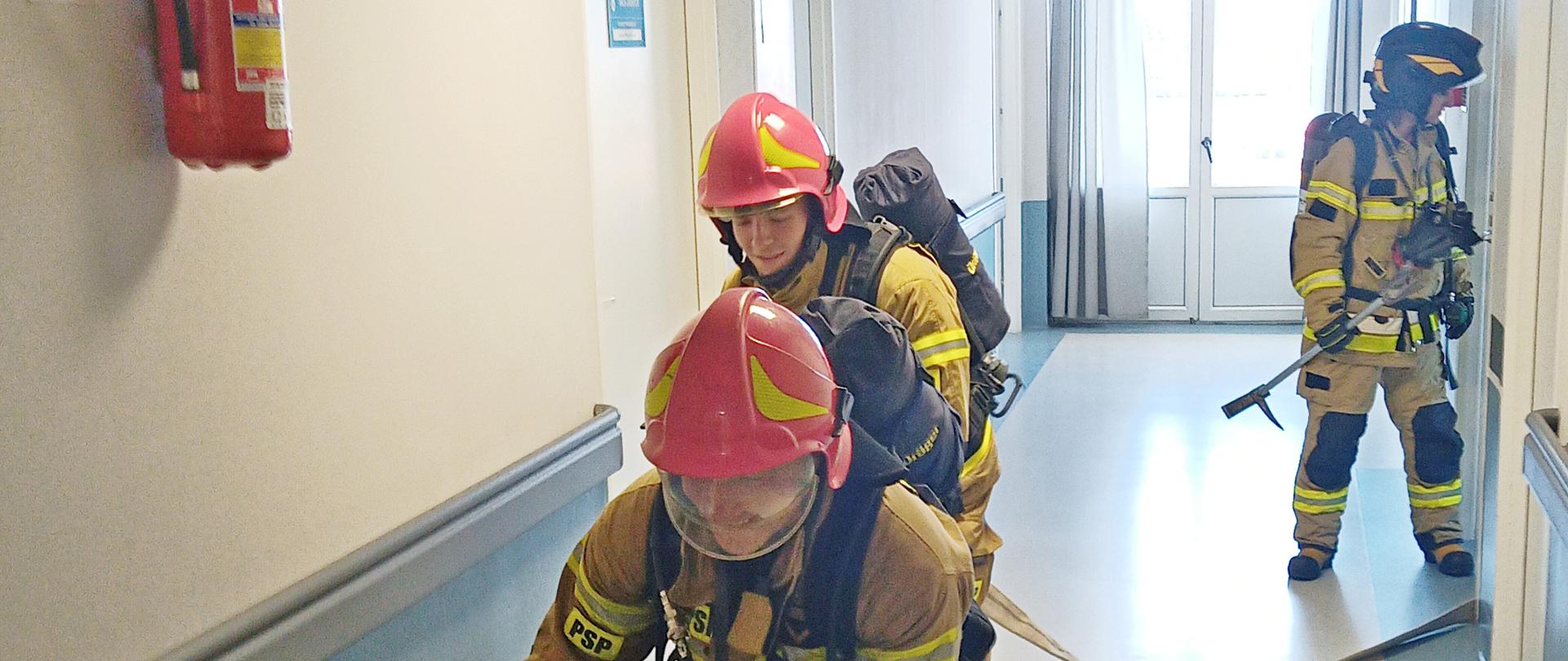 Sprawdzenie organizacji i warunków ewakuacji w budynku Szpitala Powiatowego w Sokołowie Podlaskim 2023 - strażacy w ubraniu specjalnym prowadzą rozwinięcie w budynku szpitala