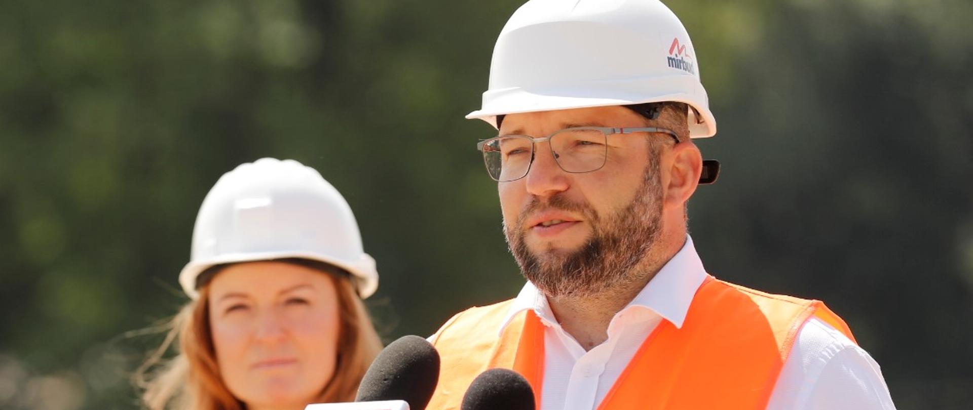 Minister Grzegorz Puda stoi przy dwóch mikrofonach i mówi.