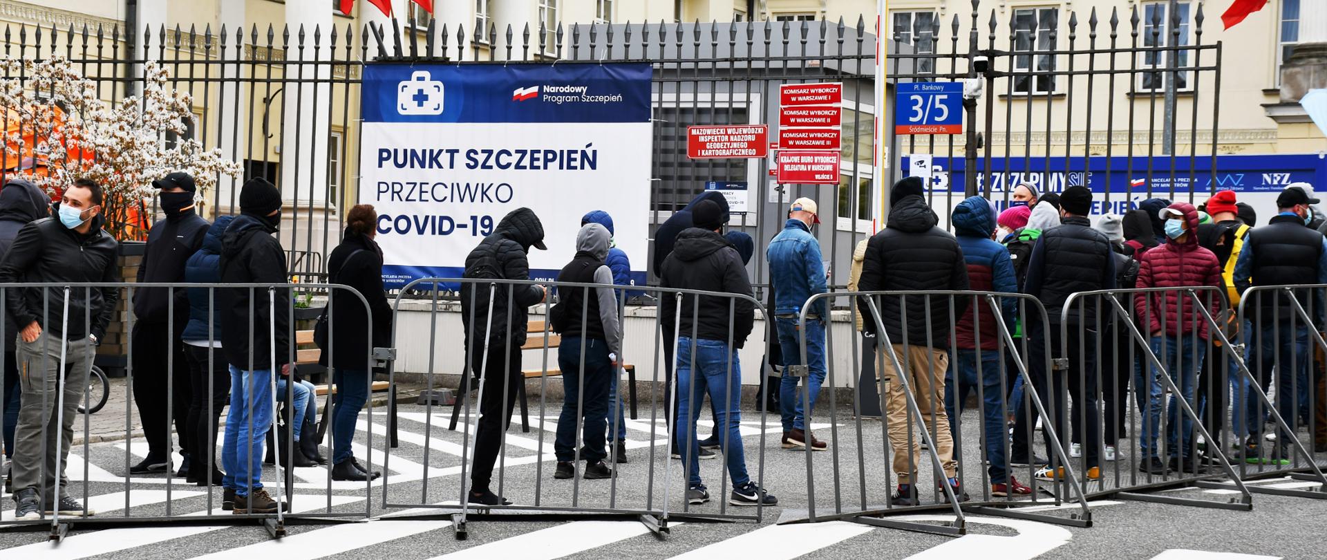 Zdjęcie przedstawia kolejkę ludzi oczekujących na szczepienie w punkcie szczepień, zlokalizowanym na dziedzińcu Mazowieckiego Urzędu Wojewódzkiego w Warszawie