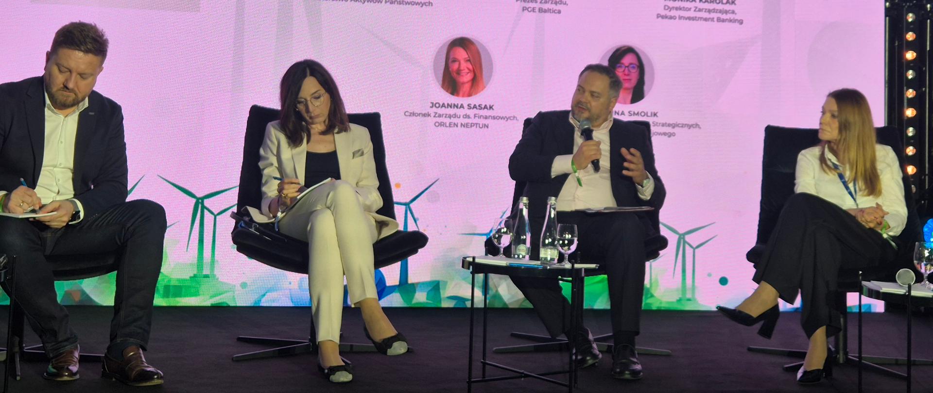 Wiceminister Konrad Gołota wraz z innymi panelistami. W tle ekran ze zdjęciami.