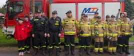 zdjęcie przedstawia strażaków jednostki w ubraniach na uroczystej zbiórce przed samochodem