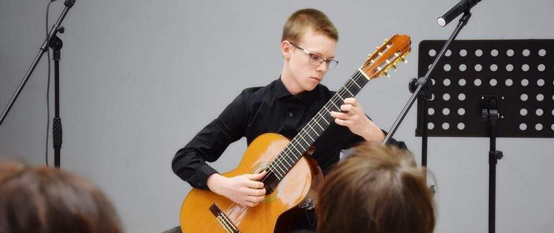 zdjęcie Sylwii Kani przedstawia Filipa Łachuta grającego na gitarze na tle szarej ściany