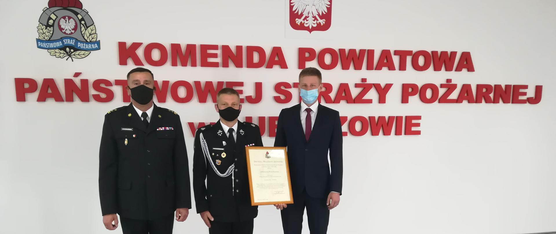 Zdjęcie przedstawia komendanta psp wraz z wójtem gminy wielkie oczy oraz prezesem osp łukawiec w tle napis komenda powiatowa psp w Lubaczowie