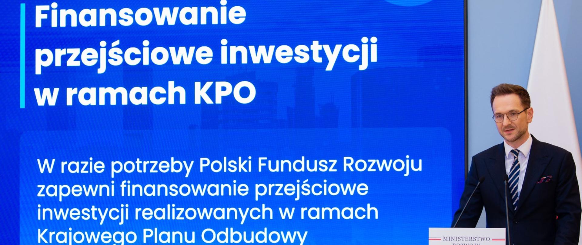 Minister Waldemar Buda na konferencji prasowej w KPRM. Na zdjęciu widać Pana ministra przed mównicą. Z tyłu widać napis związany z konferencją. 