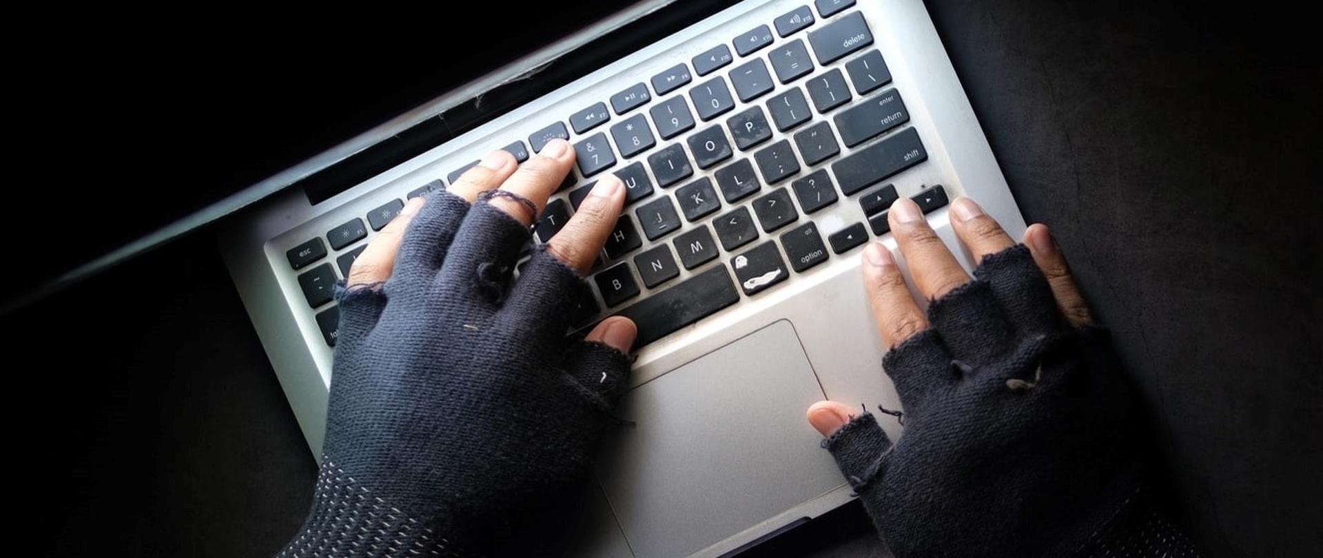 Dłonie w rękawiczkach na klawiaturze laptopa