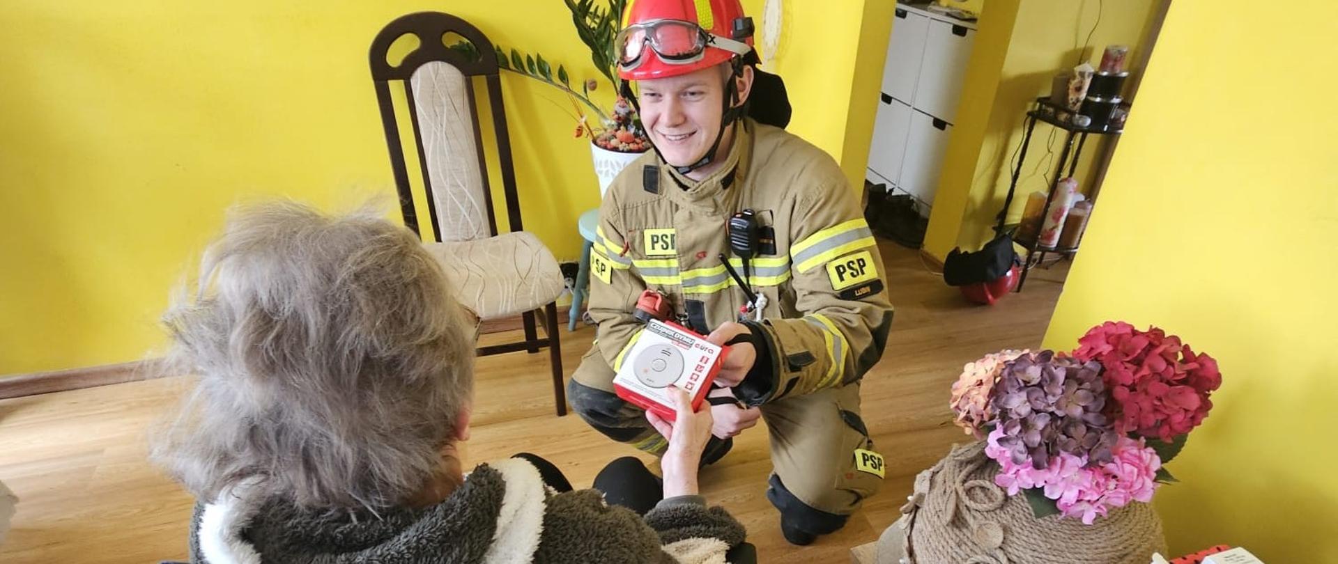 Strażak przekazuje czujkę niepełnosprawnej osobie 