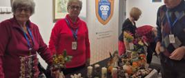na zdjęciu panie z uniwersytetu trzeciego wieku stoją przed swoim stoiskiem z rękodziełem