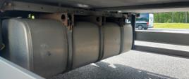 Na pierwszym planie: duży zbiornik paliwa do zasilania agregatu chłodniczego zamontowany pod naczepą ciężarową. W tle: oznakowany furgon mazowieckiej Inspekcji Transportu Drogowego.