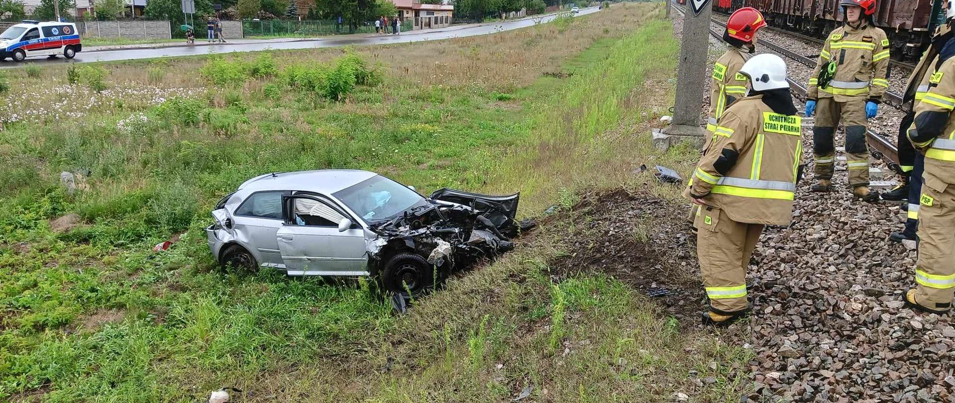 Uszkodzony samochód osobowy przy zasypie kolejowym, przy nim strażacy