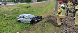 Uszkodzony samochód osobowy przy zasypie kolejowym, przy nim strażacy