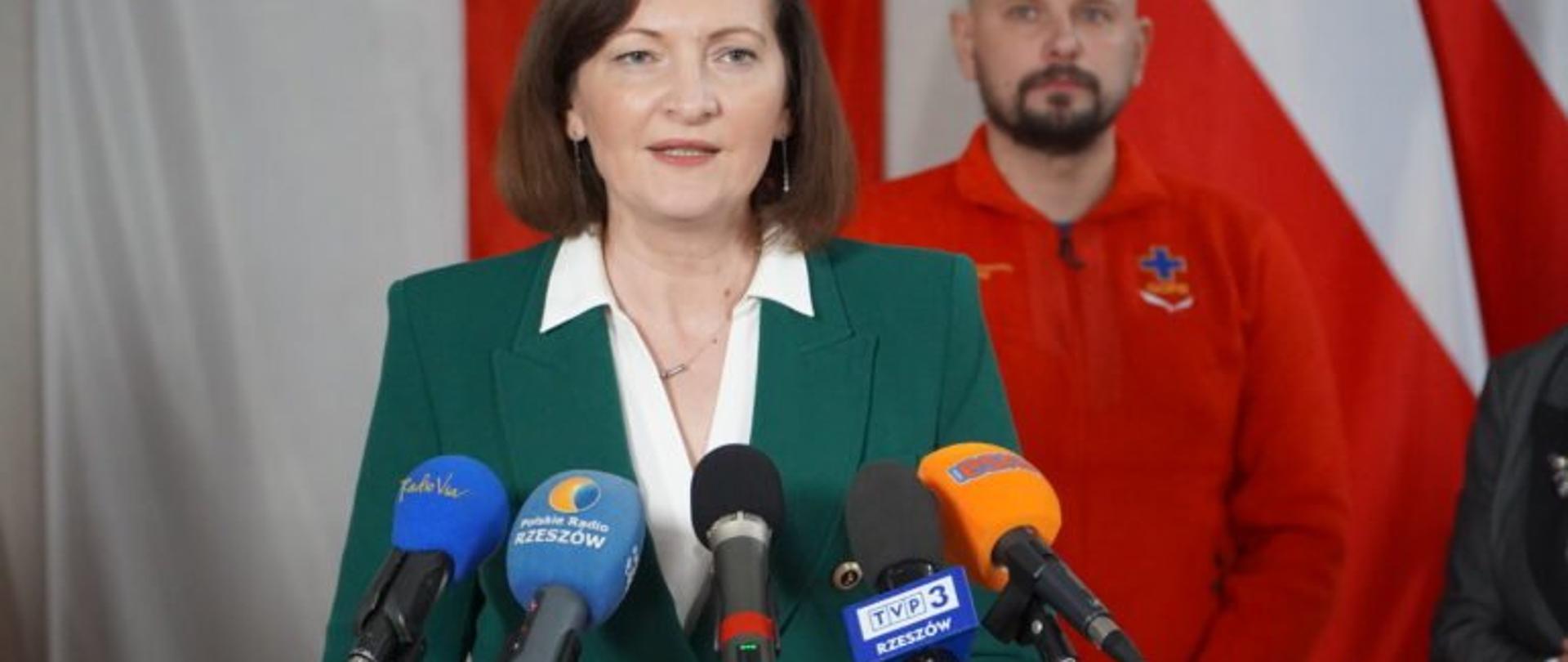 Wojewoda podkarpacki Ewa Leniart zabiera głos podczas konferencji prasowej na temat bezpiecznych ferii. W tle stoi zastępca naczelnika Bieszczadzkiej Grupy GOPR Jakub Dąbrowski.