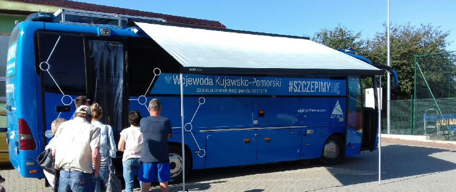 Na zdjęciu szczepionkobus w gminie Drzycim. Po lewej stronie zdjęcia osoby czekające w kolejce do zaszczepienia się.