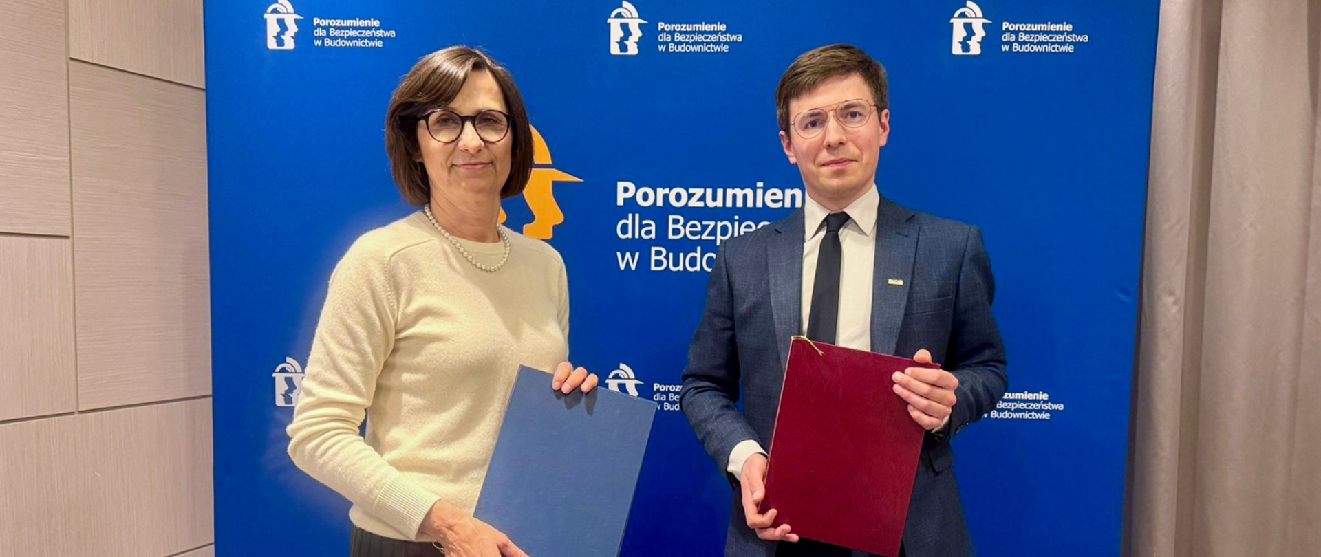 Na zdjęciu od prawej: Filip Prusik-Serbinowski, Zastępca Głównego Inspektora Nadzoru Budowlanego i Małgorzata Winiarek-Gajewska, Prezydent Porozumienia dla Bezpieczeństwa w Budownictwie pozują trzymając w rękach teczki z podpisanym porozumieniem.