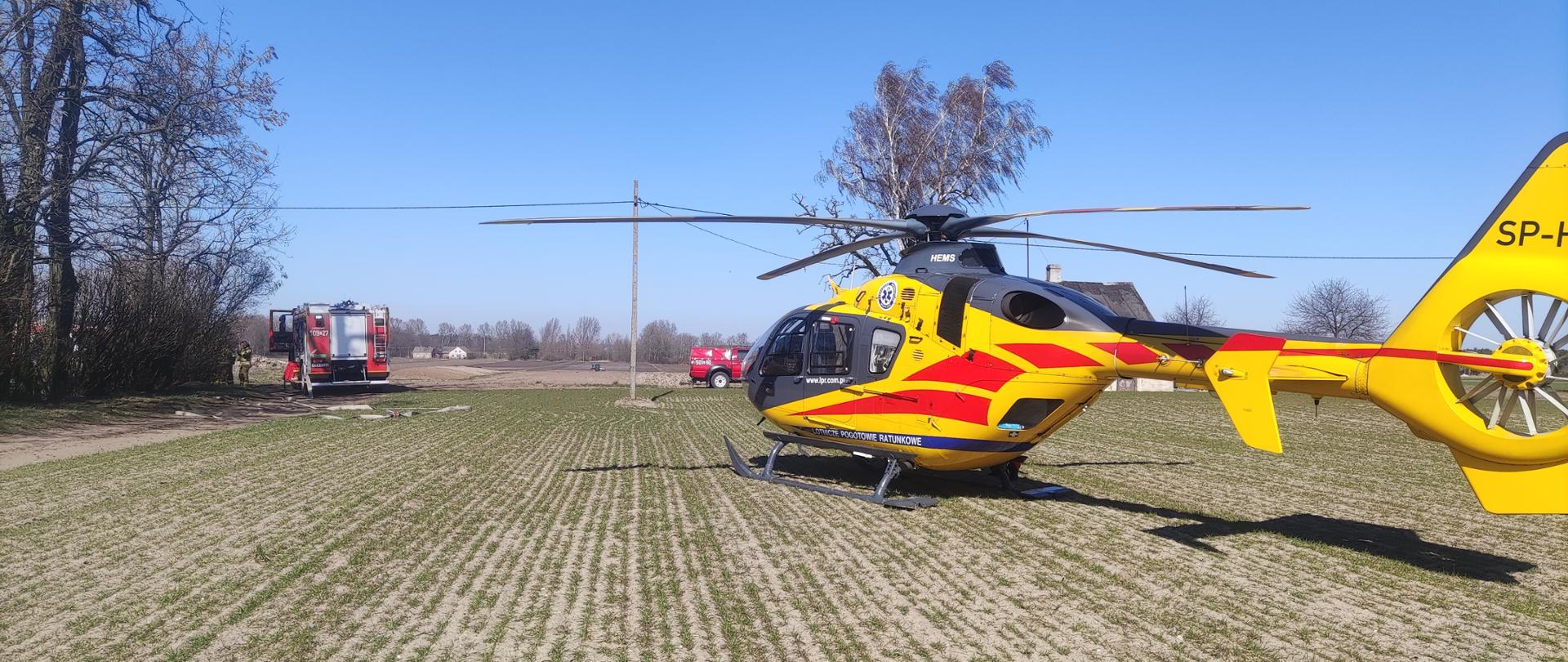 Zdjęcie przedstawia zabezpieczenie lądowania Lotniczego Pogotowia Ratunkowego, na pierwszym planie śmigłowiec LPR, na drugim wóz strażacki oraz samochód rozpoznawczo-ratowniczy