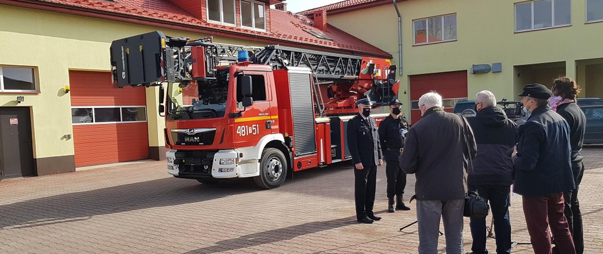 Na zdjęciu widzimy Komendanta Powiatowego PSP w Skarżysku-Kamiennej st. bryg. Marcina Machowskiego oraz jego Zastępcę st. kpt. Marcin Jasińskiego podczas prezentacji otrzymanego samochodu z drabiną mechaniczną mediom z terenu powiatu skarżyskiego. Komendant opisuje możliwości taktyczno-bojowe nowoczesnego sprzętu