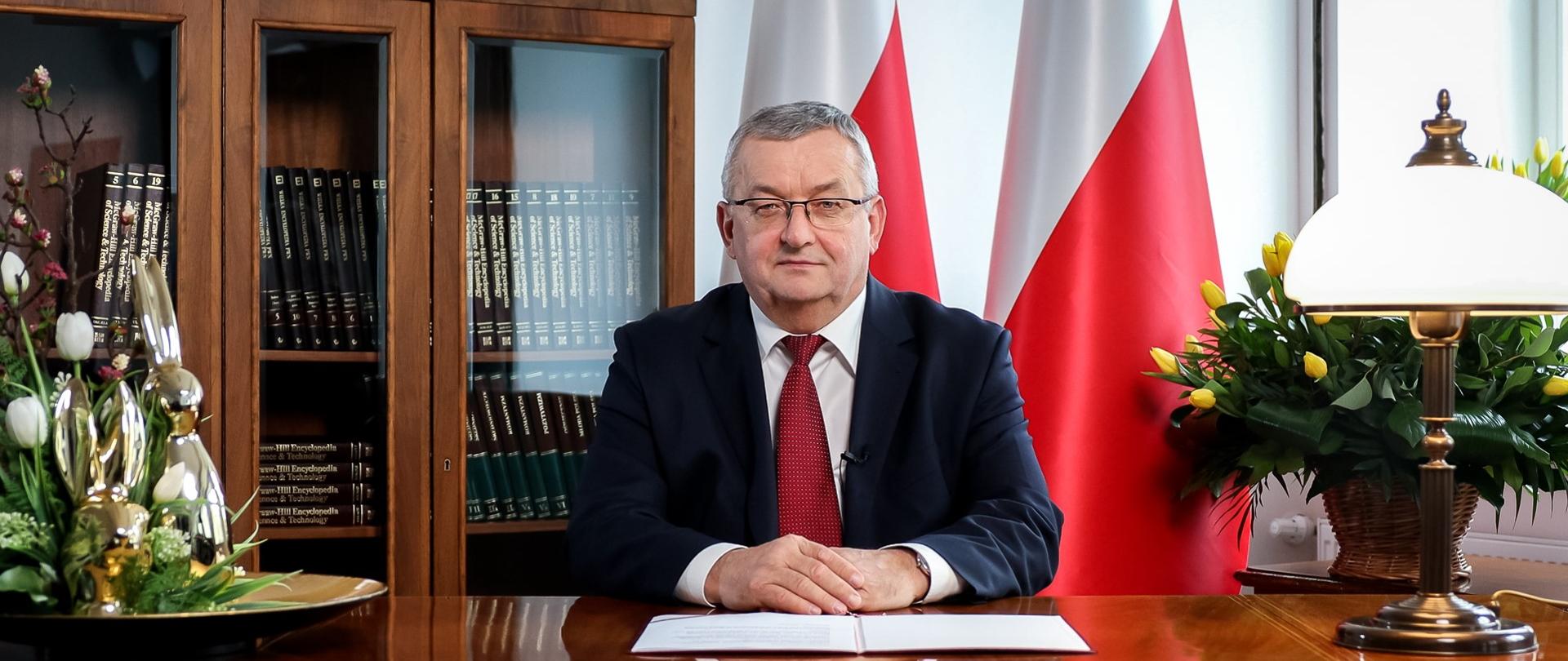 Minister infrastruktury Andrzej Adamczyk na tle flag RP