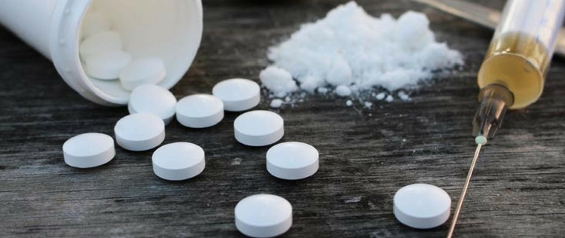 Zdjęcie przedstawia różnego rodzaju środki psychoaktywne w formie tabletek, proszku oraz w płynnej postaci podawanej poprzez strzykawki.